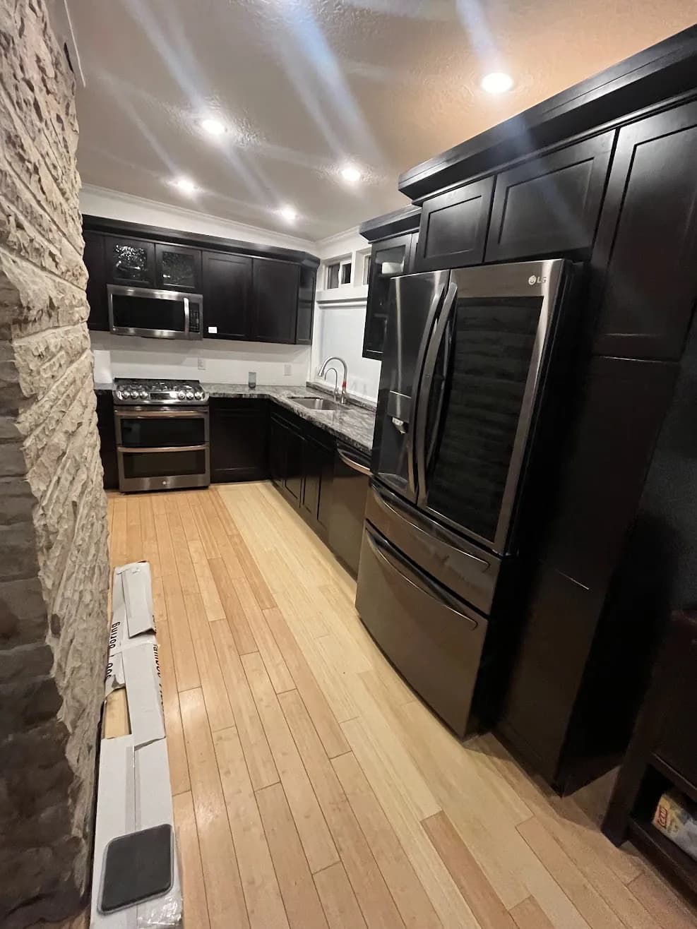 Completed kitchen reconstruction with dark cabinetry, stone accent wall and new hardwood flooring