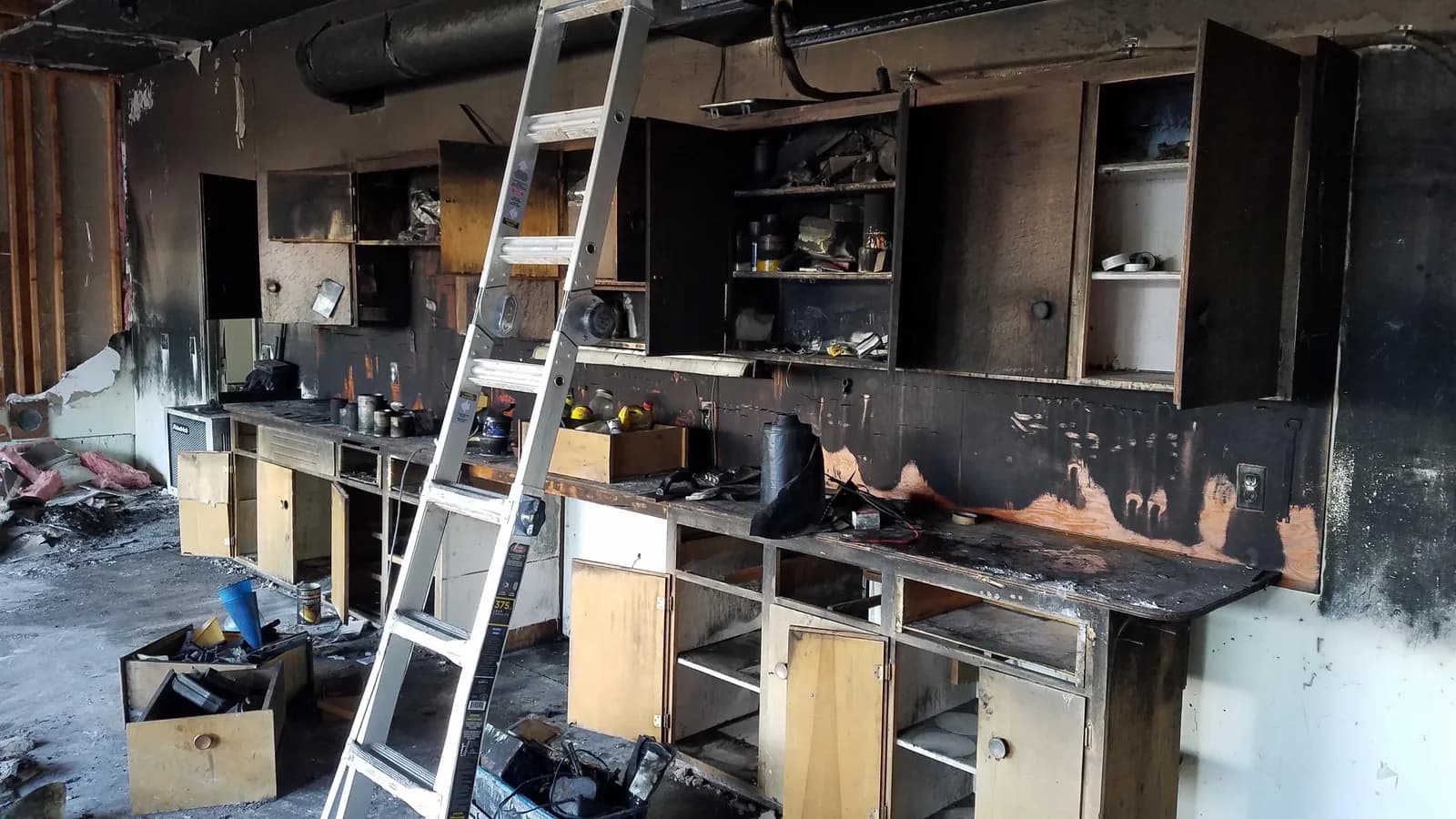 Kitchen gutted by fire with charred cabinets and blackened walls, ladder in place for assessment