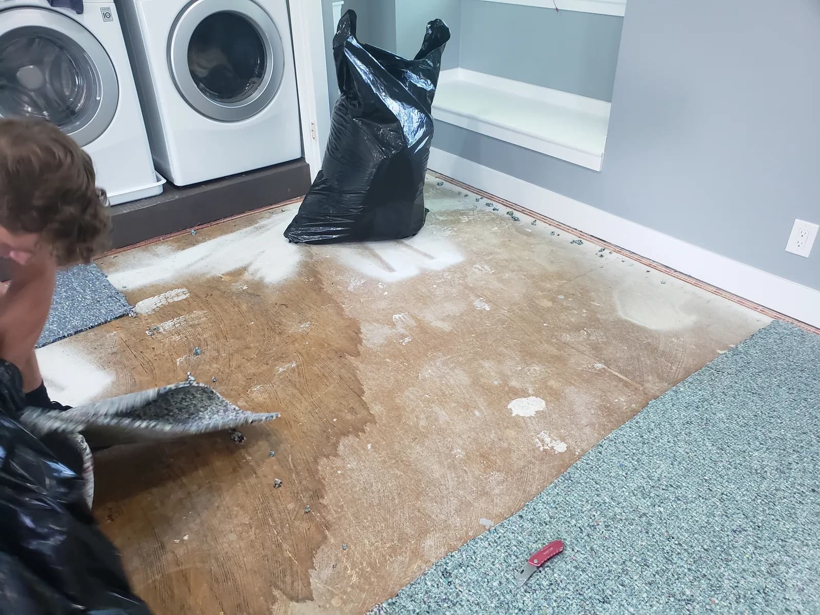 Water-damaged laundry room with saturated carpet and padding being cut out and bagged for disposal