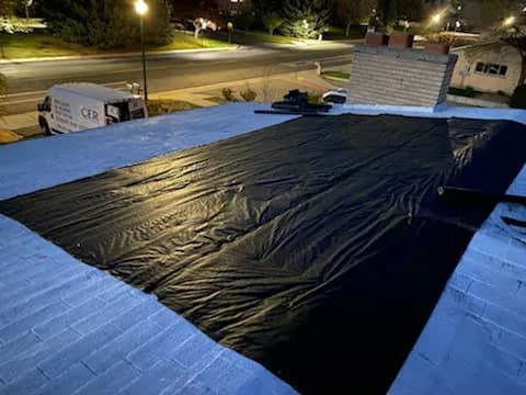 Emergency tarp installed over a storm-damaged roof at night to stop further water intrusion